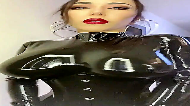 Japanese Mistress Youko's shiny latex catsuit hugs her huge boobs as she dominates her submissive